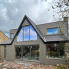 Modern house with antique slatted composite cladding, large windows and a sloped roof against a cloudy sky.