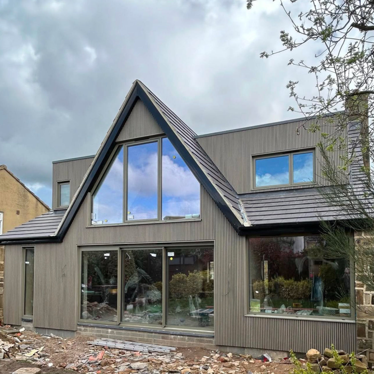 Modern house with antique slatted composite cladding, large windows and a sloped roof against a cloudy sky.