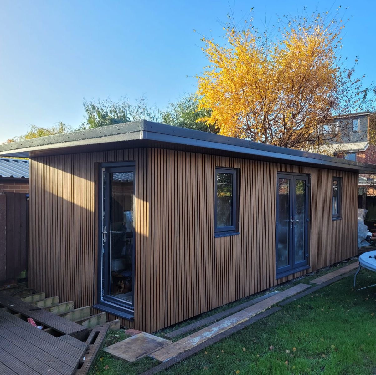 Composite slatted cladded garden room with large windows in a backyard setting