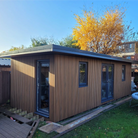 Composite slatted cladded garden room with large windows in a backyard setting