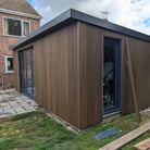 Modern garden shed with composite slatted cladding in Golden Teak exterior and glass doors, surrounded by a garden.