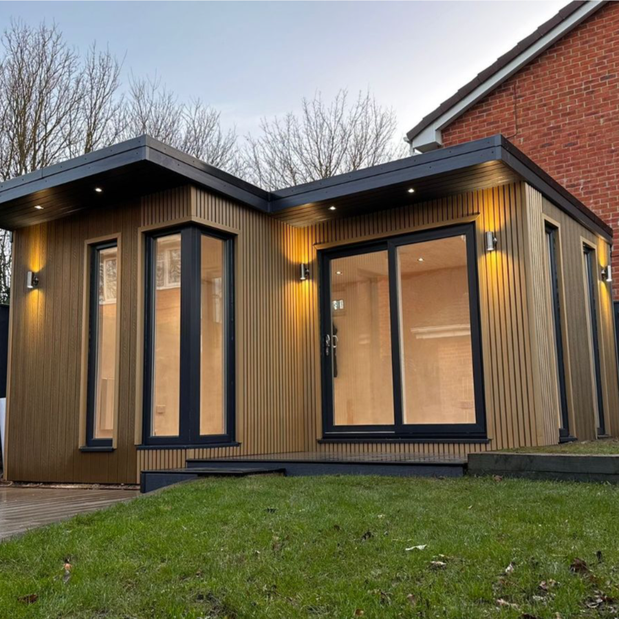 Modern house extension with a composite slatted cladded exterior and large windows, set against a brick wall.