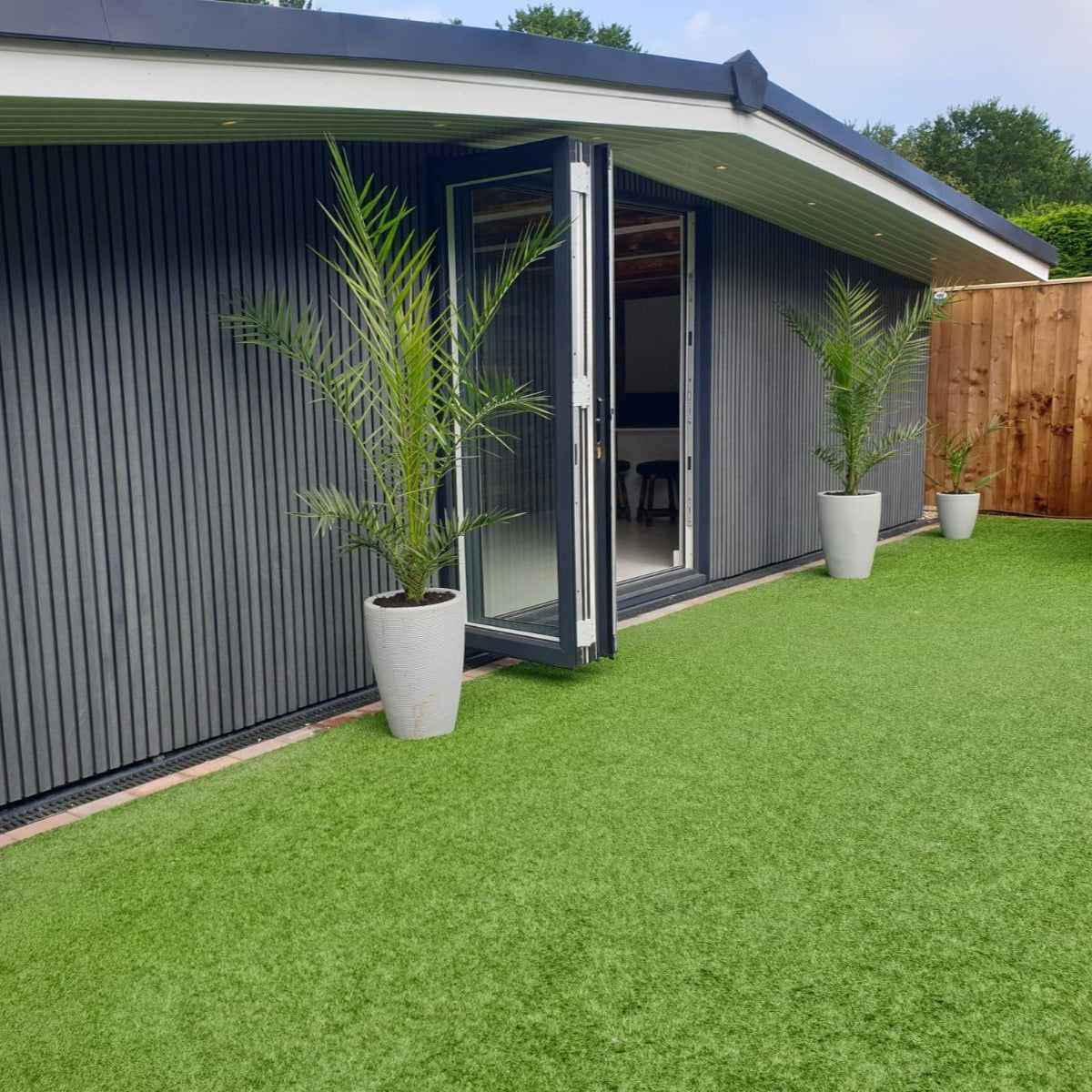 Modern house exterior with green lawn, potted plants, and a wooden fence.