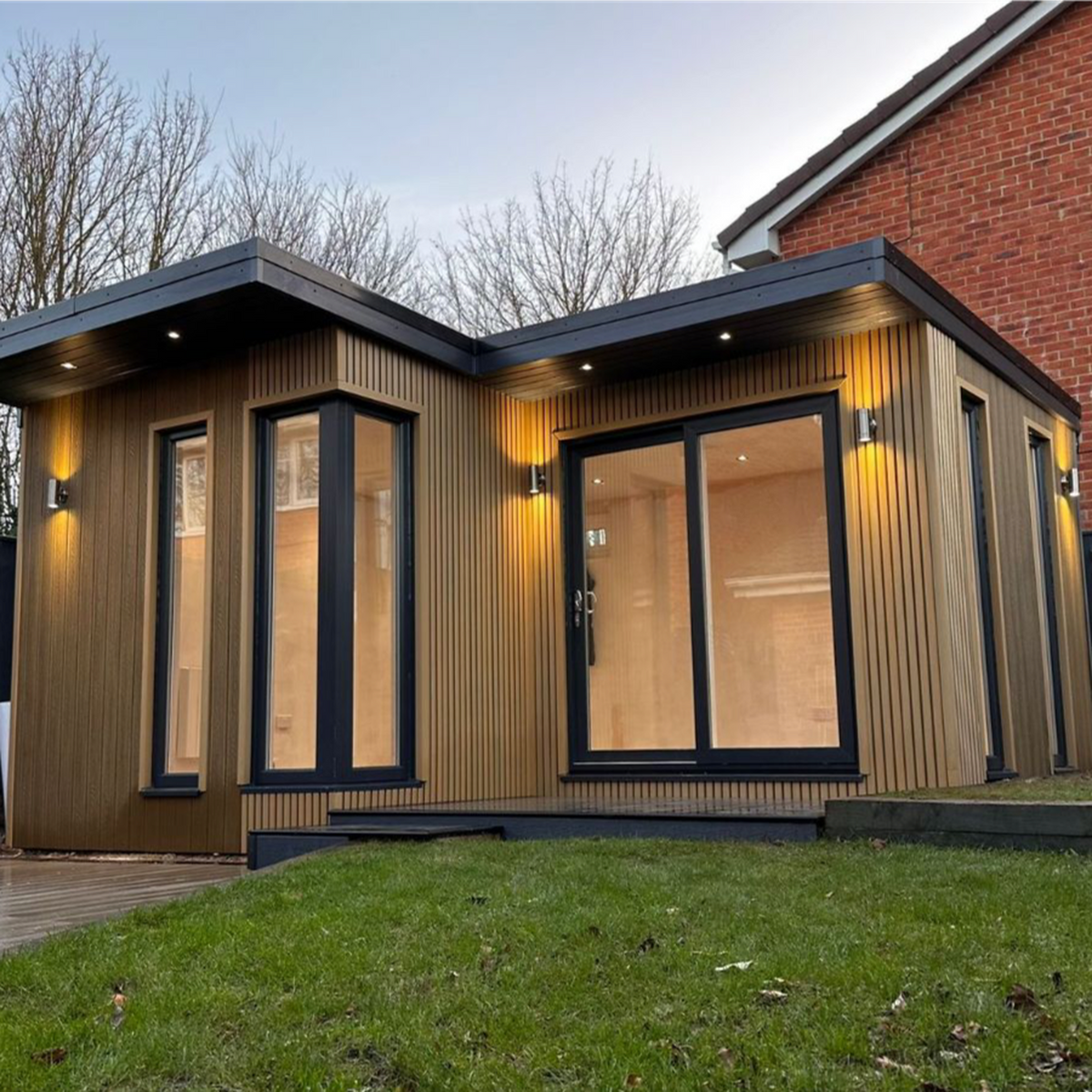 Modern house extension with a composite slatted cladded exterior and large windows, set against a brick wall.